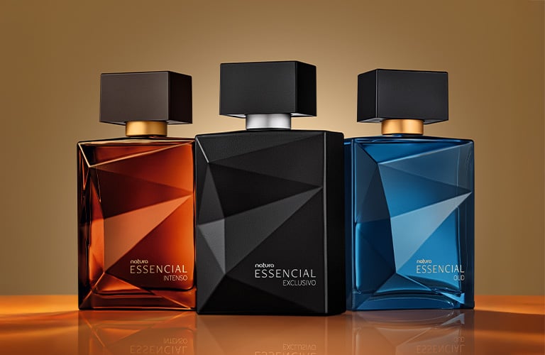 Foto de tres frascos de perfume Essencial de Natura, en colores ámbar, negro y azul, con diseño geométrico, sobre una superficie brillante color marrón.
